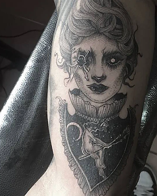 Retrato ilustrado de mujer con una araña en el ojo y una bruja sobre la luna, en negro con puntillismo, en el brazo