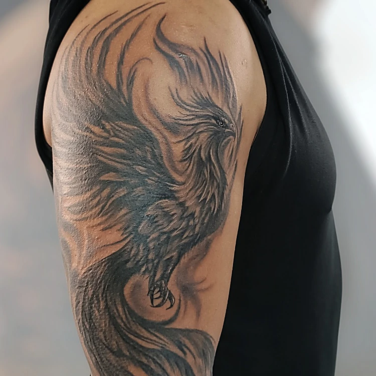 Fénix en negro y gris con alas abiertas en el brazo