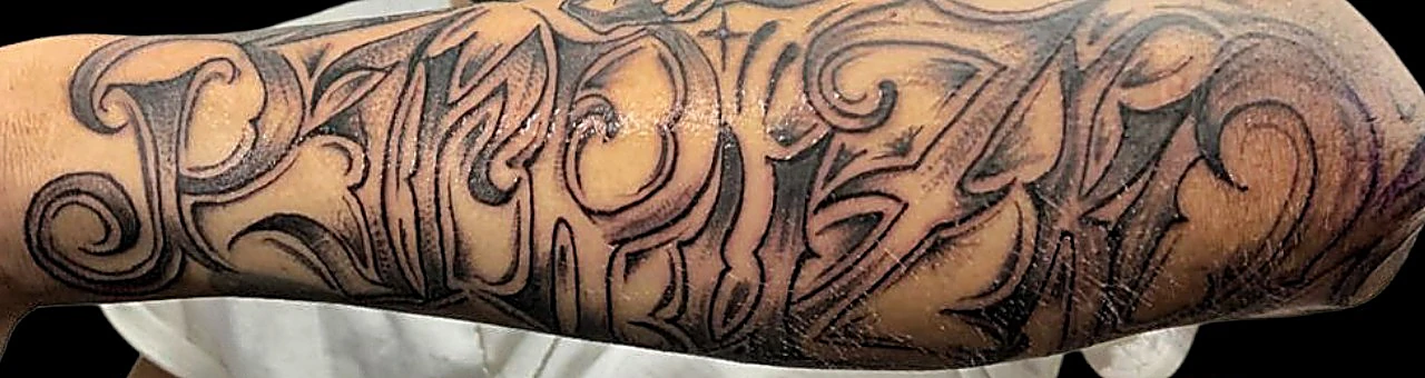 Lettering de trazo grueso y ornamentado a lo largo del antebrazo