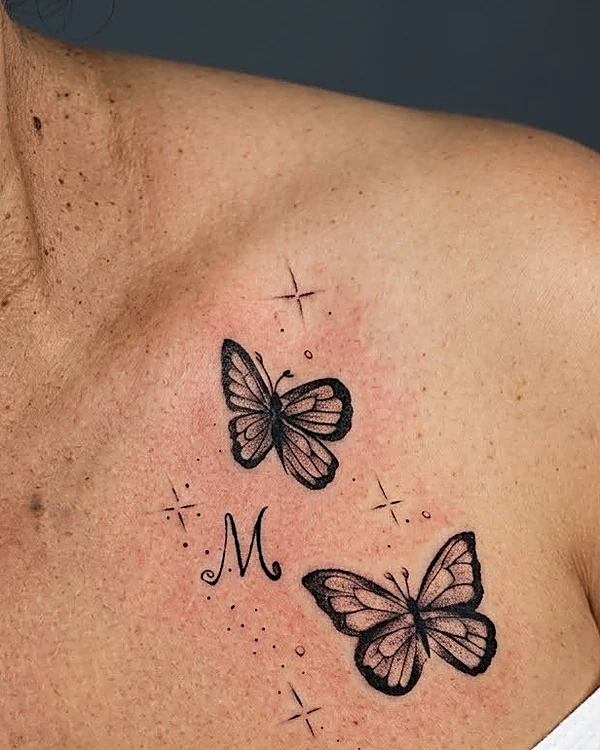 Dos mariposas en línea fina con una letra M y destellos en la clavícula